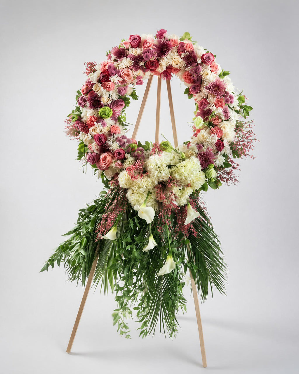 Floral wreath with pink, white, and green flowers on a stand against a gray background