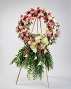 Floral wreath with pink, white, and green flowers on a stand against a gray background