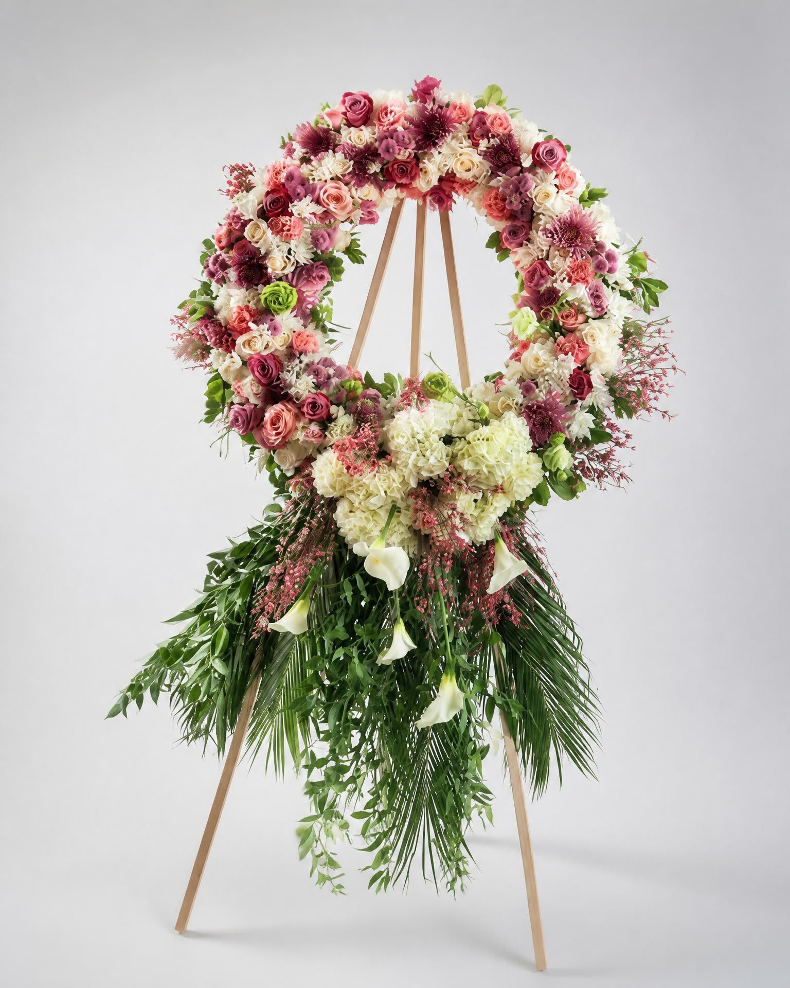 Floral wreath with pink, white, and green flowers on a stand against a gray background
