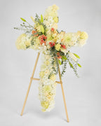 Floral cross arrangement on a stand against a light gray background