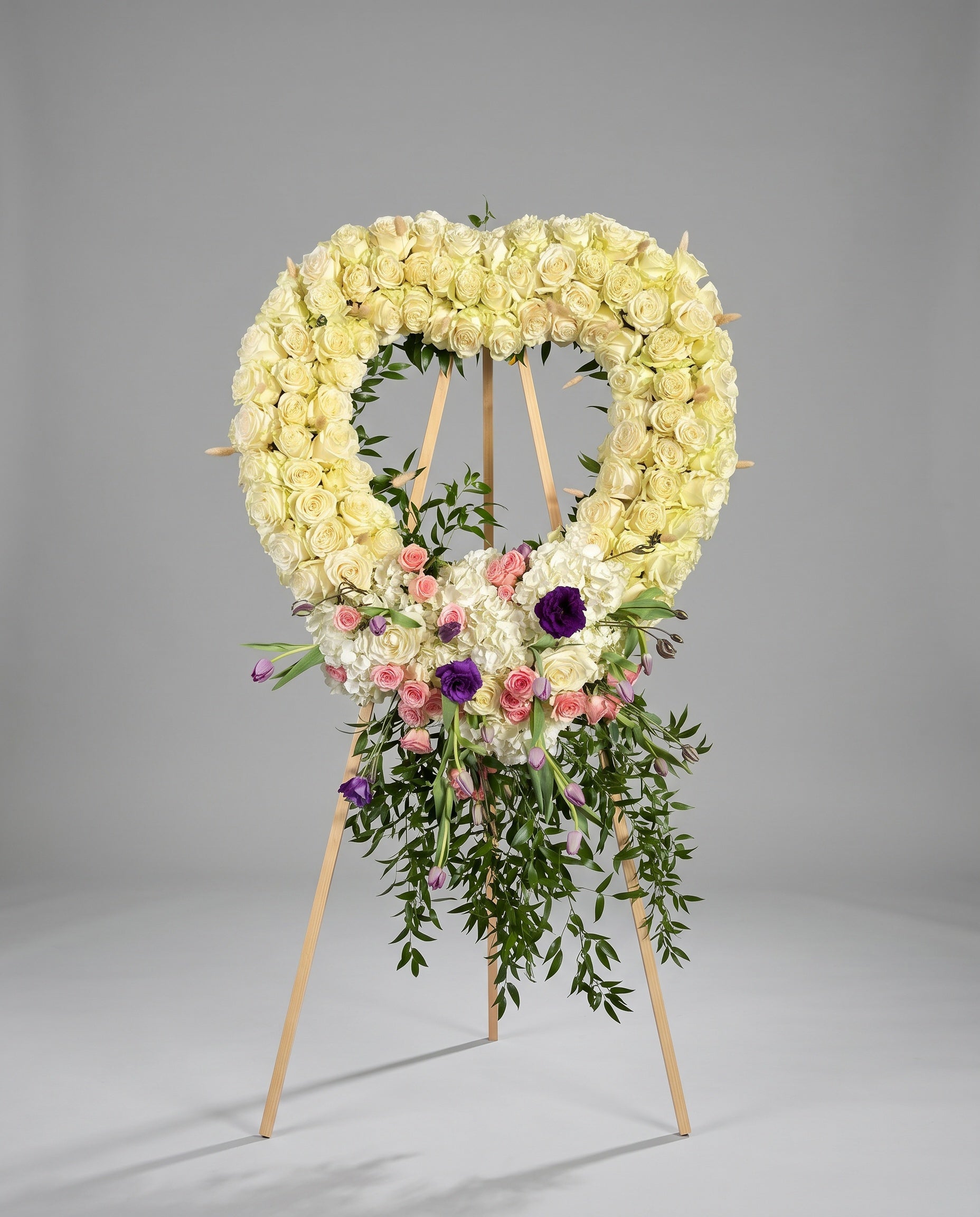 Heart-shaped floral arrangement with white, pink, and purple flowers on a gray background