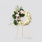 Floral wreath with white and green flowers on a stand against a light gray background