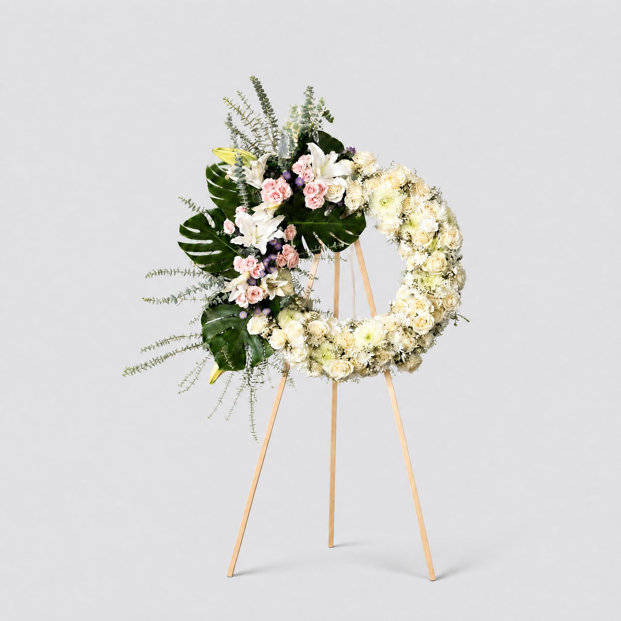 Floral wreath with white and green flowers on a stand against a light gray background